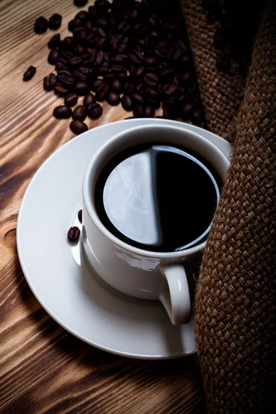 Café frijoles y café en taza blanca sobre mesa de madera con arpillera — Foto de Stock