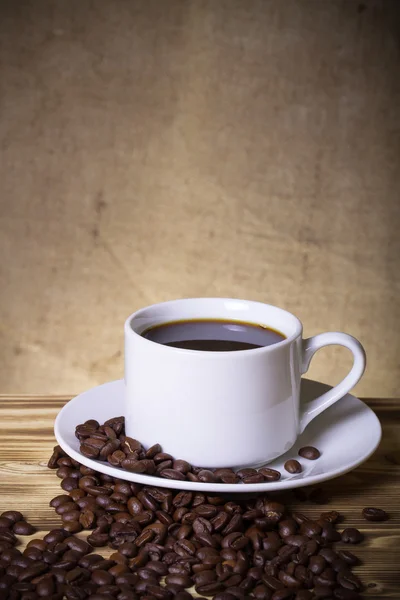 Granos de café y café en taza blanca en la mesa de madera frente a un — Foto de Stock