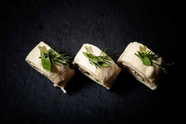 Små rullar med skinka, ost och pita på spett på en svart skiffer — Stockfoto
