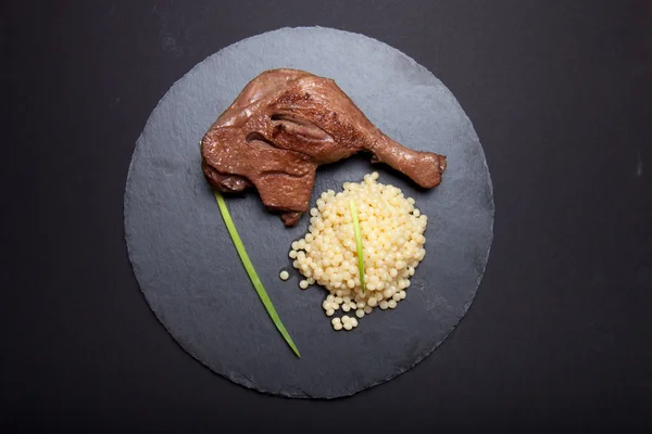 Bebek kaki dengan couscous di piring batu tulis hitam — Stok Foto