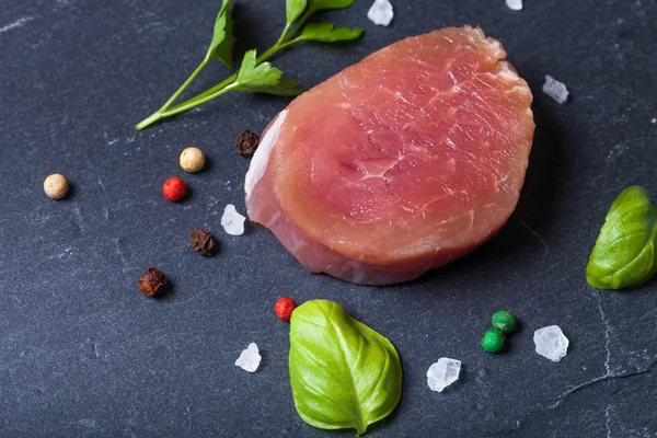 Raw meat with herbs and spices on a black slate plate — Stock Photo, Image