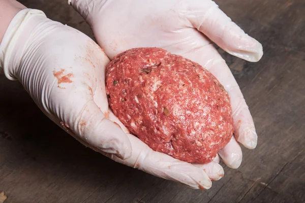 Hand in glove holding a raw cutlet — Stock Photo, Image