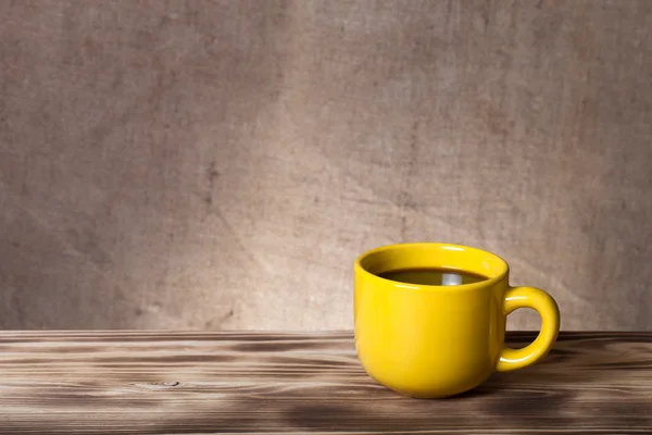 Caffè in tazza sul tavolo di legno di fronte a uno zaino di iuta sfocato — Foto Stock