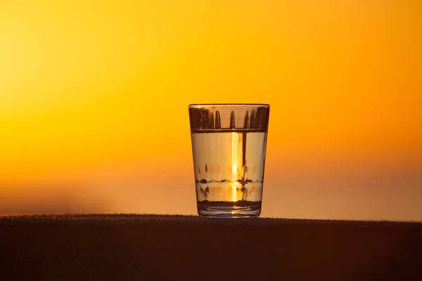Glass of water on the background of beautiful sunset. Selective — Stock Photo, Image