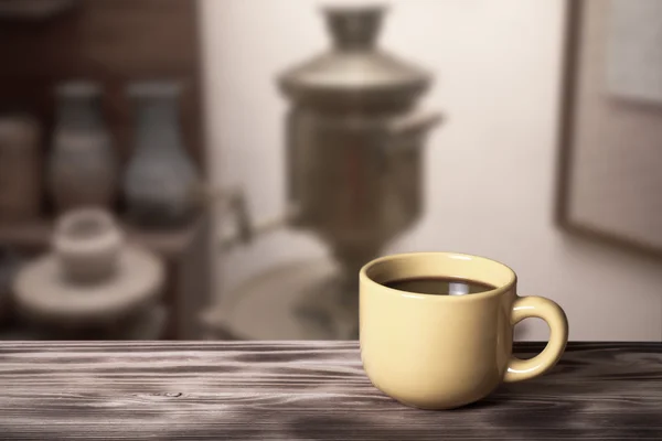 Café en una taza sobre mesa de madera frente a un desenfocado el interio — Foto de Stock