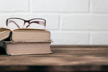 Çevrimdışı eğitim kavramı okuma öğrenme bilgeliği, görme bozukluğu, açık kitap ve gözlükler tahta bir masanın üzerinde fotokopi alanı olan beyaz tuğla duvar arka planına karşı..