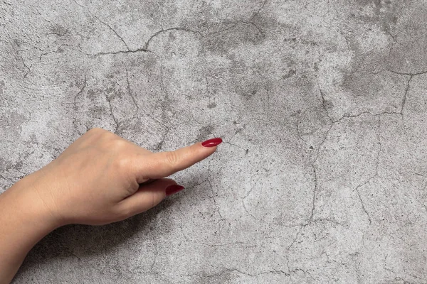 一只有红指甲的雌性手的食指指向混凝土墙的中心，背景为人体的一部分，并复制空间 — 图库照片