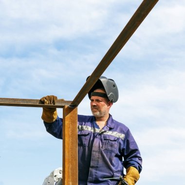 Bir endüstri işçisi inşaatçıdır, erkek kaynakçı koruyucu bir kaynak maskesiyle çalışır, metal bir yapı yapar..