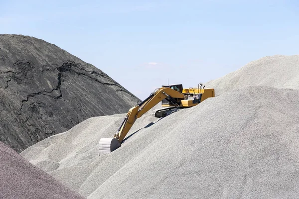 Industria, trattore escavatore con un secchio lavora sulla cima di un mucchio di ghiaia in un impianto di asfalto in un cantiere in una fossa aperta — Foto Stock