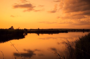 Günbatımı turuncu dramatik gökyüzü ile gölün üzerinde, yaz mevsiminde gölün kıyısında balık tutmak.