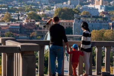 Gürcistan, Tiflis - 24 Ekim 2020: Üç kişilik aile güzel bir günde şehir manzarasının keyfini çıkarıyor.