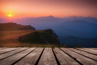 Güzel yaz arkaplanı, dağların ardında gün batımı ve doğada boş ahşap masa. Doğal şablon manzarası.