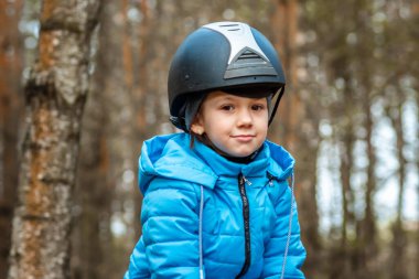 Doğanın arka planında kahverengi bir atın üstünde küçük bir kız. Jokey, epodrom, ata binme