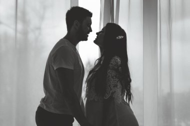 Kocasıyla birlikte hamile bir kız parlak bir yatak odasında duruyor. Genç, çekici, hamile bir kızın güzel göbeği. Aile, evlilik, doğum kavramı