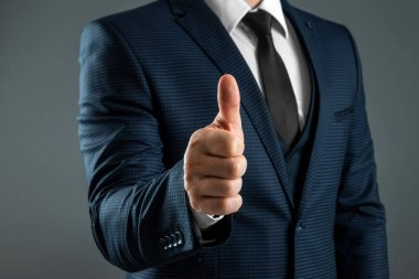 Takım elbiseli erkek, gri arka planda olumlu bir hareket gösteriyor. Konsept tamam, onay, yakın çekim