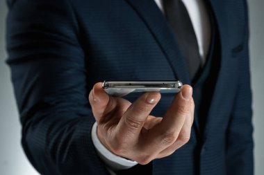 Takım elbiseli bir işadamı akıllı telefonu elinde tutuyor. Ortaklarla çalışmak ve iletişim kurmak için interneti kullanıyor. Çevrimiçi iş konsepti, uzaktan çalışma, serbest çalışma