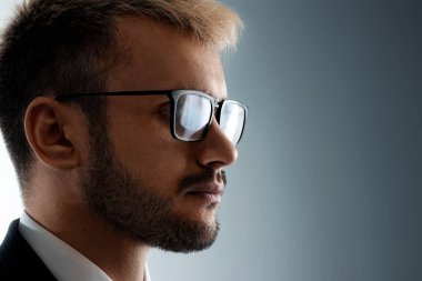 Gözlüklü bir adamın yakın plan portresi. Profilde, karanlıktan gelen ışığa bakıyor. Nötr yüz ifadesi, boşluğu kopyala