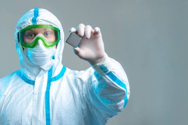 Bir çalışan elinde bir mikroçip tutuyor koruyucu bir takım elbise, gözlük, maske ve eldiven takıyor. En son teknolojiler, elektronik mikro devre, bilgisayar güvenliği, sinirsel ağlar