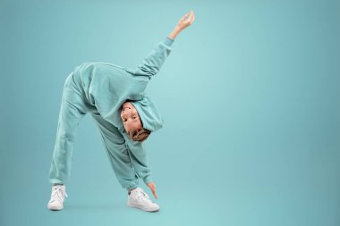 Turkuaz kıyafetli küçük bir kız poz veriyor ve turkuaz arka planda aylaklık ediyor, kameraya bakıyor. Çocuk stüdyo resmi. Çocukluk yaşam tarzı konsepti