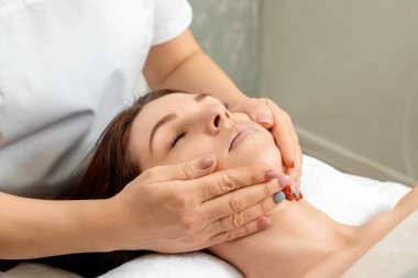 Yüz masajı yakın plan. Spa prosedürlerinde genç ve güzel bir kız. Cilt bakımı, oryantal masaj tedavileri, güzellik tedavileri