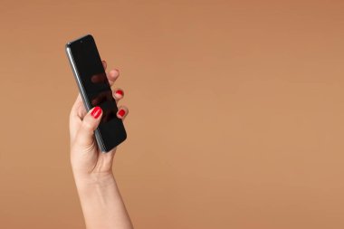 Bir kadının elinde bej arka planda bir akıllı telefon.