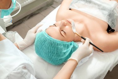 Güzellik uzmanı bir güzellik salonunda yüzüne maske takar. Yüz temizliği, kozmetik prosedürleri, cilt bakımı, cilt gözenek temizleme, donanım kozmetolojisi