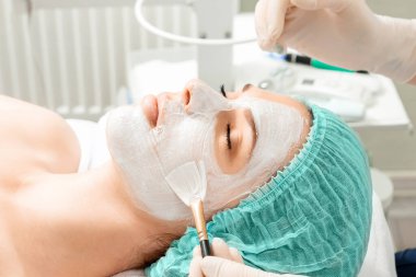 Güzellik uzmanı bir güzellik salonunda yüzüne maske takar. Yüz temizliği, kozmetik prosedürleri, cilt bakımı, cilt gözenek temizleme, donanım kozmetolojisi