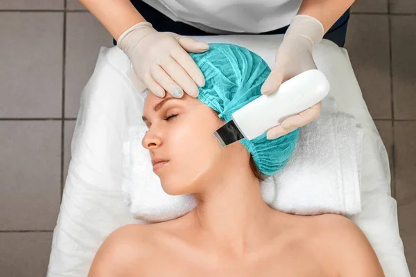 A gloved beautician cleanses the skin on the face using a special gel and equipment. The concept of facial hygiene, cosmetic procedures, skin care, skin pore cleansing, hardware cosmetology