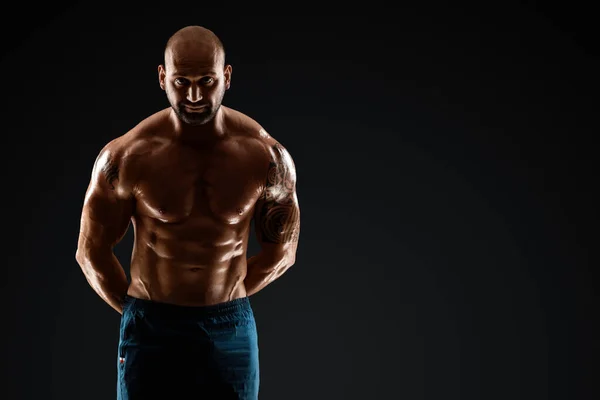 Tattooed male bodybuilder posing over black background. Fitness workout concept, muscle groups, watch your body