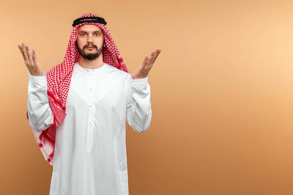 An Arab man in national dress is praying on a beige background. Dishdasha, kandora, thobe ,, traditional men's clothing of the Middle East, islam, faith. Copy space
