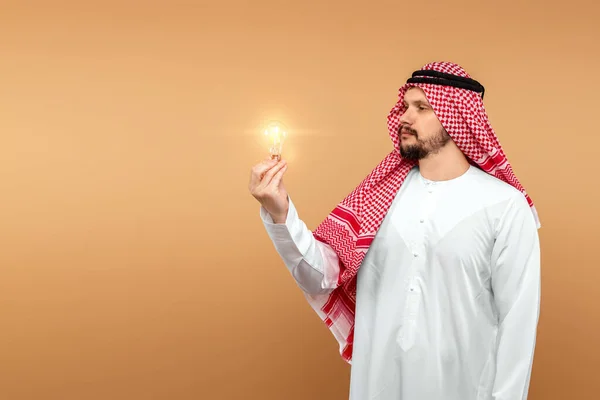 Arabski Mężczyzna Trzyma Narodowy Kostium Żarówką Ręku Beżowym Tle Pomysł — Zdjęcie stockowe