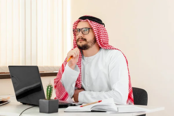 An Arab man, a businessman, a sheikh works at a laptop. Investments, business, work via the Internet, online contracts