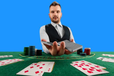 Kumarhanedeki erkek krupiye mavi arka planda tek başına. Kumarhane konsepti, kumar, poker, yeşil kumarhane masasında çip