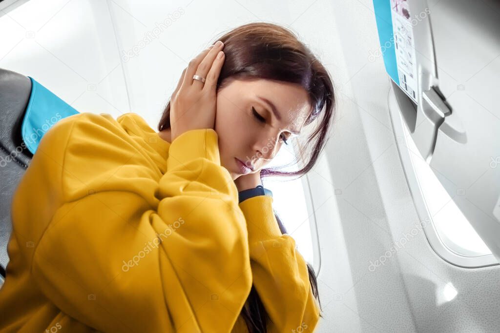 A girl sits in front of an airplane window and is nervous, afraid to fly, the cabin of a passenger airliner. Aerophobia, phobia, international flights, stress, motion sickness
