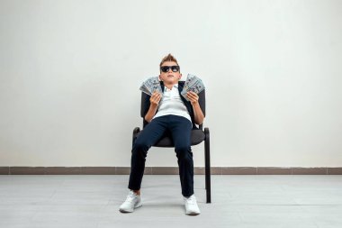 Hafif bir geçmişi olan zengin bir çocuk elinde bir tomar para tutuyor. Finansal eğitim, genç milyoner, yatırımlar, krediler, kazançlar, kâr payları. Boşluğu kopyala