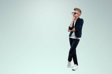 Takım elbiseli bir çocuk beyaz bir arka planda dalgın duruyor.