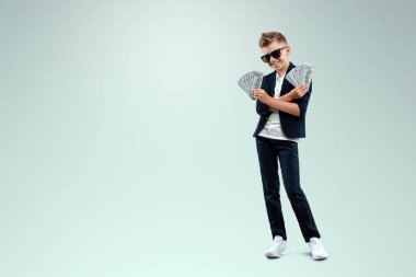 Gözlüklü zengin bir çocuk, düşen banknotların arka planına karşı dolar tutuyor. Nasıl para kazanılacağını biliyor. Para yağmuru, mali eğitim, genç milyoner, yatırımlar, krediler, kazançlar