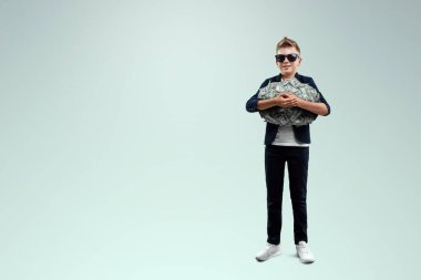 Gözlüklü zengin bir çocuk, düşen banknotların arka planına karşı dolar tutuyor. Nasıl para kazanılacağını biliyor. Para yağmuru, mali eğitim, genç milyoner, yatırımlar, krediler, kazançlar