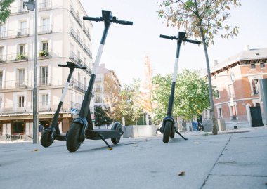 Güneşli bir günde Madrid 'de caddeye park edilmiş çağdaş elektrikli scooterların alçak açısı.