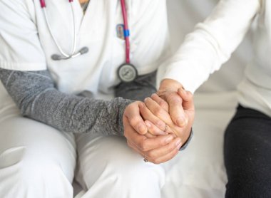 Kanepede yan yana otururken yaşlı bir kadının elini tutan yüksek açılı isimsiz doktor.