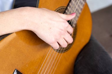 Stüdyoda müzik sırasında manikürlü, akustik gitar çalan isimsiz bir kadından.