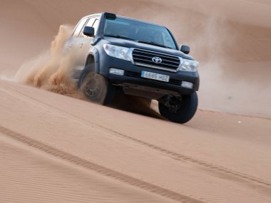 Siyah bir Toyota 4x4 'ün yüksek hızda keskin kum tepeciklerinden aşağı düşüşünü, tekerleklerin Fas Sahra Çölü' nde devasa altın kum bulutlarını savuruşunu..