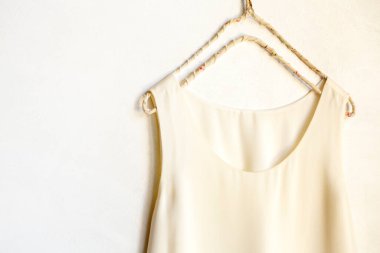 Beyaz bir duvardaki askıda asılı bej ya da beyaz bir atlet. Kapat ve boşluğu kopyala.