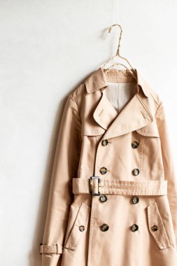 Beyaz bir duvarda asılı duran bej renkli trençkot. Kapat ve boşluğu kopyala.