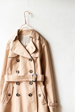 Beyaz bir duvarda asılı duran bej renkli trençkot. Kapat ve boşluğu kopyala.