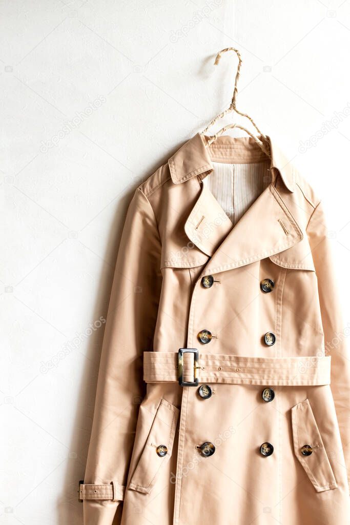 Beige trench coat isolated hanging on a hanger in a white wall. Close up and copy space.