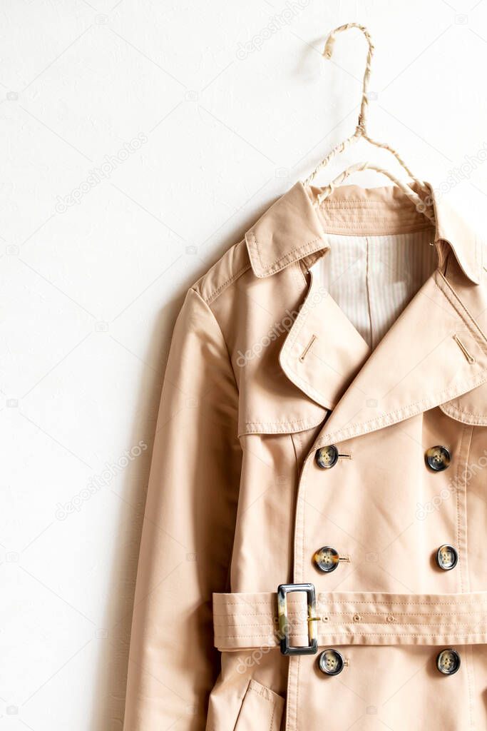 Beige trench coat isolated hanging on a hanger in a white wall. Close up and copy space.