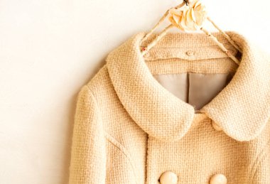 Elbiselerde asılı bej renkli yün palto. Beyaz arka planda asılı. Kapat..