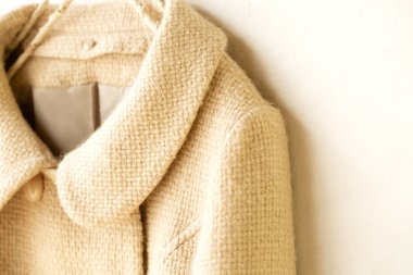 Elbiselerde asılı bej renkli yün palto. Beyaz arka planda asılı. Kapat..