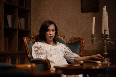 Genç Asyalı kadın eski lüks koltukta oturuyor.